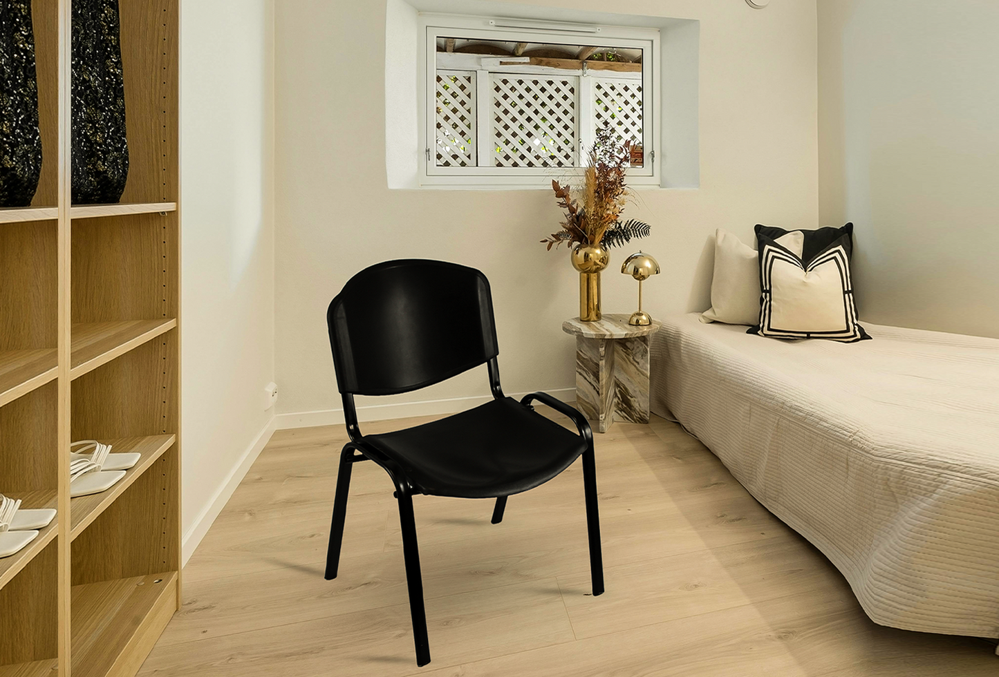 Black Meta Furniture Plastic Stacking Chair placed in a modern bedroom with light wood flooring and beige bedding